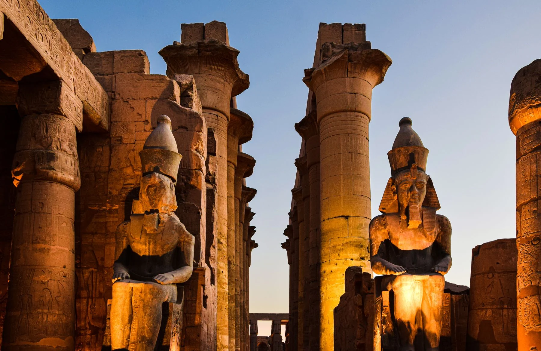 Colossal statues and illuminated columns at Luxor Temple as evening falls